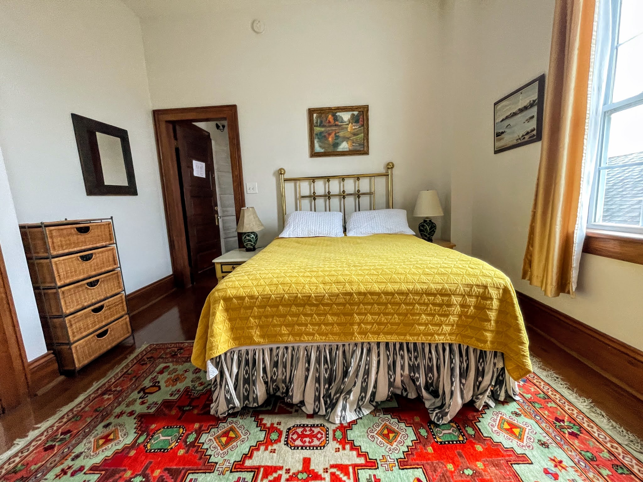 A wide view of a bedroom with a yellow bedspread, white pillows, and a colorful rug.