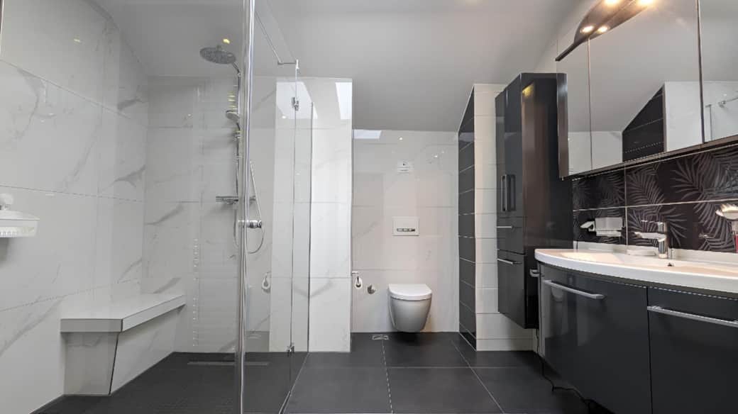 Unser großzügiges Gemeinschaftsbad verfügt über eine ebenerdige Regendusche sowie Fußbodenheizung für höchsten Komfort. Die moderne Ausstattung sorgt für ein luxuriöses und angenehmes Badeerlebnis.