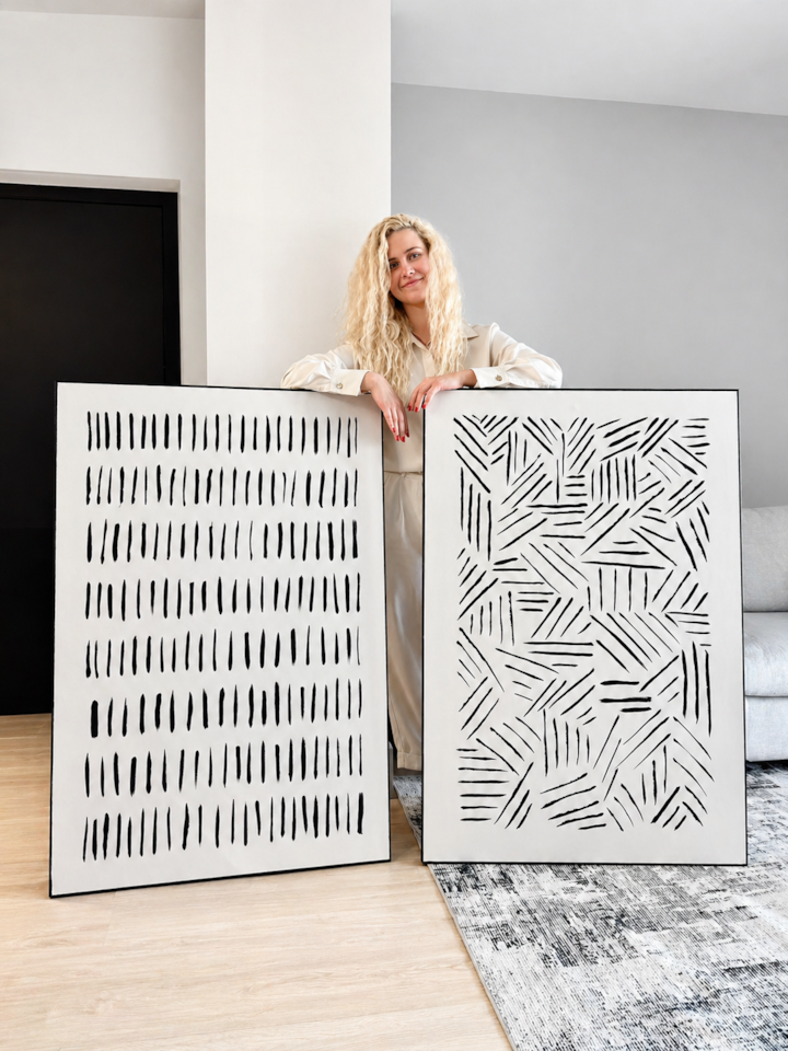 Anastasia Duke standing inside AZULIS Apartments #7 in Olbia, presenting her two original paintings — Fragmented Paths and Quiet Intervals — on the walls for the first time, April 2026