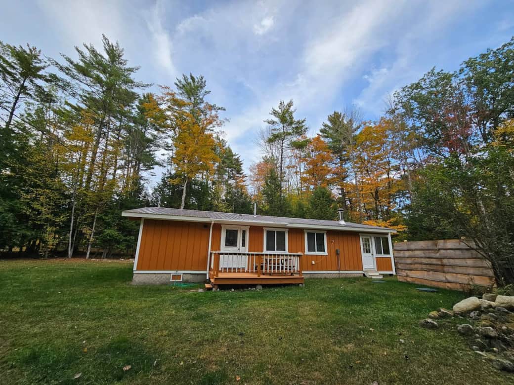 Charming cabin with porch and private yard, nestled in the forest with vibrant fall colors—perfect retreat for nature lovers.
