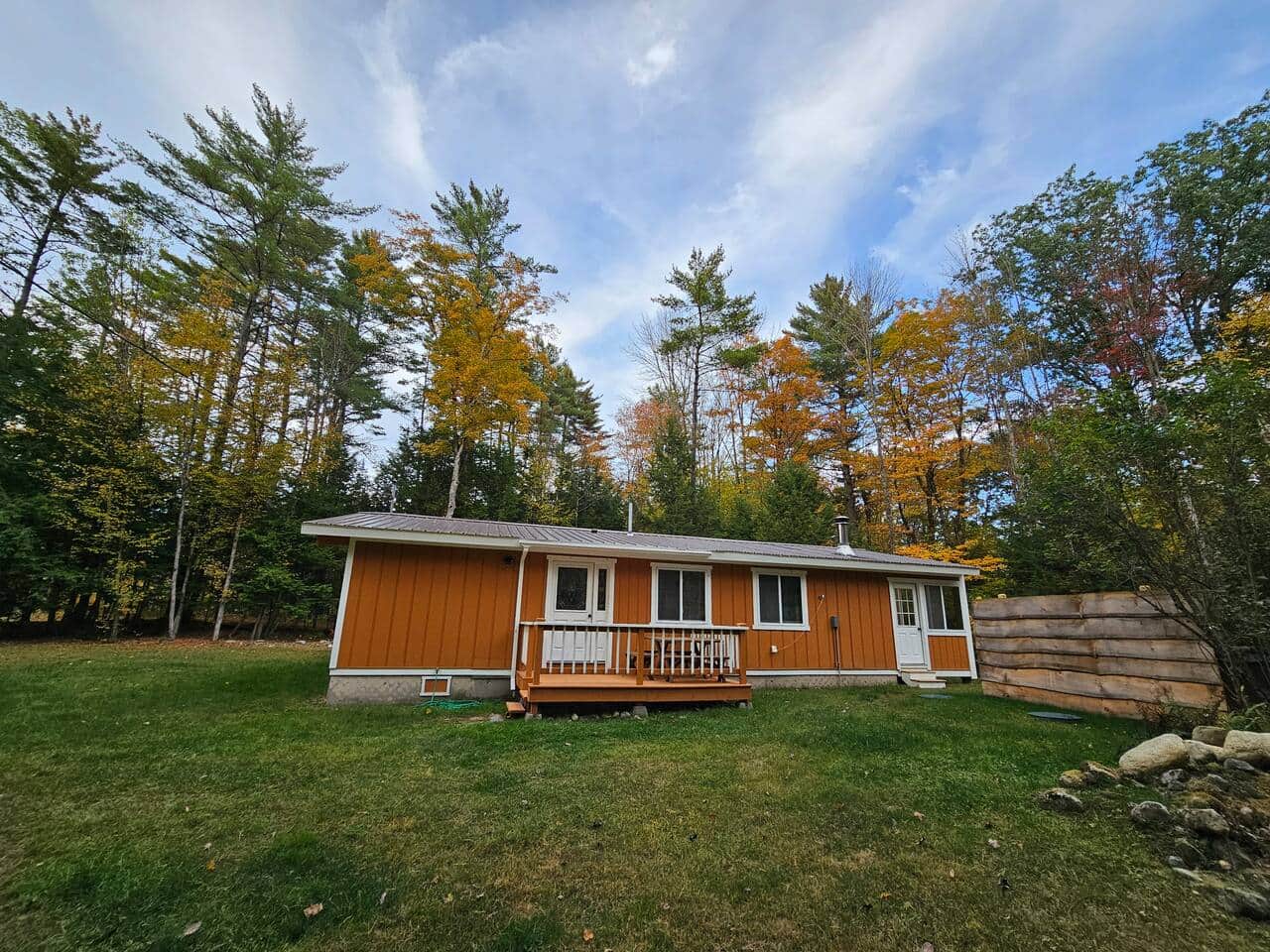 Charming cabin with porch and private yard, nestled in the forest with vibrant fall colors—perfect retreat for nature lovers.