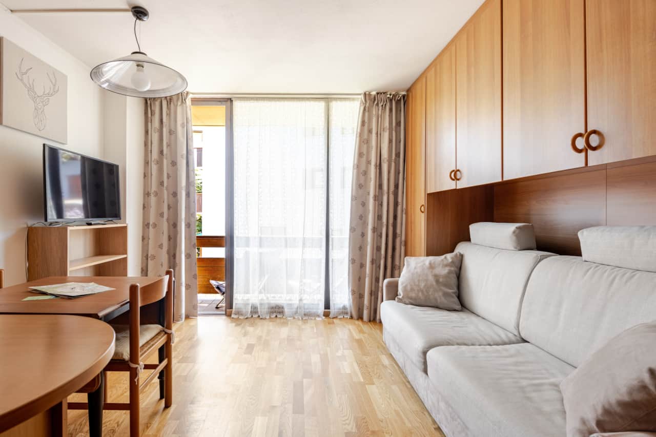 Wohnzimmer mit hellem Sofa, TV und Holzverkleidung