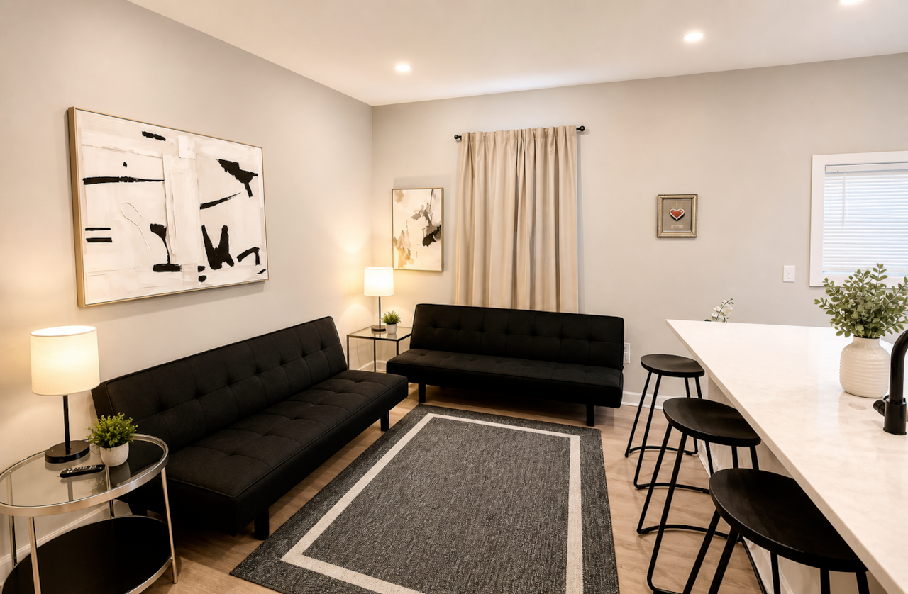 Stylish  living space featuring two futon sofa beds, a flat-screen TV, and a modern electric fireplace. The large island bar offers generous seating and flows into the kitchen, creating a comfortable space to relax, dine, or entertain.