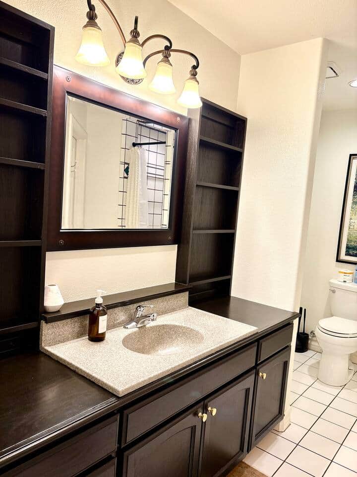Master bedroom en suite bathroom with sage green walls and white tile accents. Spacious vanity, framed mirror with a built-in shelving, and walk-in shower. Clean lines and ample storage space.