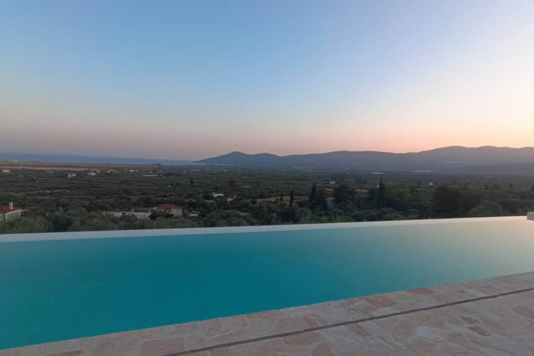 At sunset, the infinity pool melts into the horizon, reflecting soft pastel skies over the olive plain and distant hills. The landscape feels serene and timeless - a peaceful invitation to unwind and embrace the beauty of Mediterranean evenings.