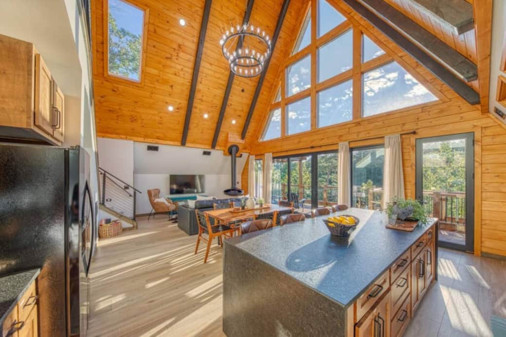 The large windows will bring you closer to nature. A large luxury hanging trumpet-shaped fireplace, a spacious open floor plan, and a large black iron chandelier really set the mood for a perfect space for you to relax or entertain.