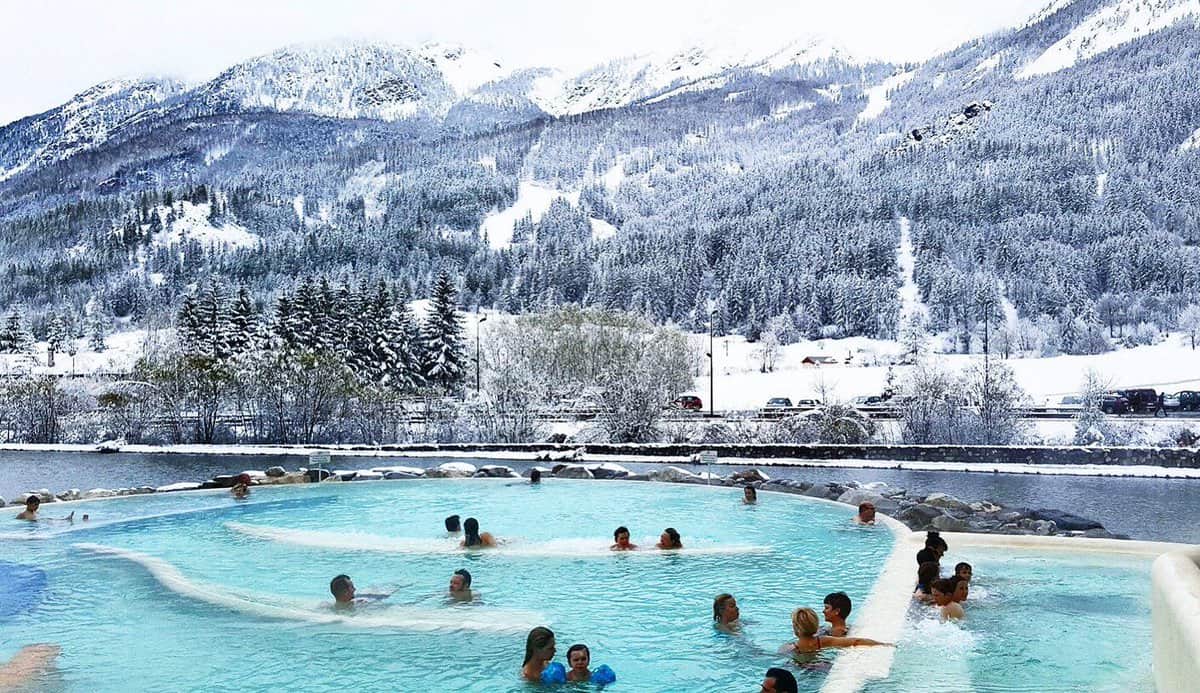 Baigneurs dans la piscine extérieure des Grands Bains du Monêtier face à la forêt enneigée, Serre Chevalier Vallée