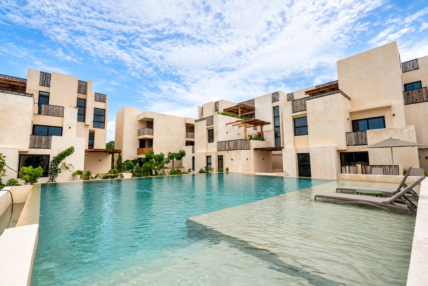 Otra de las 4 albercas infinity de Gran Tulum, con amplia zona para nadar, camastros dentro del agua y sombrillas: perfecta para refrescarte bajo el sol de Tulum.
