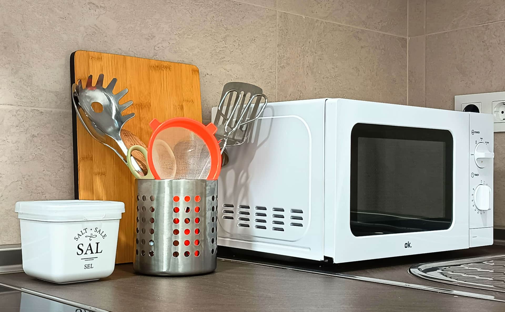 Encimera de cocina con microondas, utensilios de cocina, recipiente de sal y tabla de cortar en La Casita de Ale