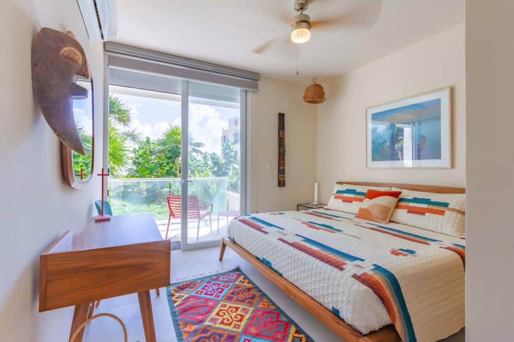 Cozy and colorful bedroom with a king-size bed, air conditioning, ceiling fan, and room-darkening shades. Enjoy lush garden views and direct access to your private terrace with beautiful ocean views—perfect for a peaceful night’s rest.