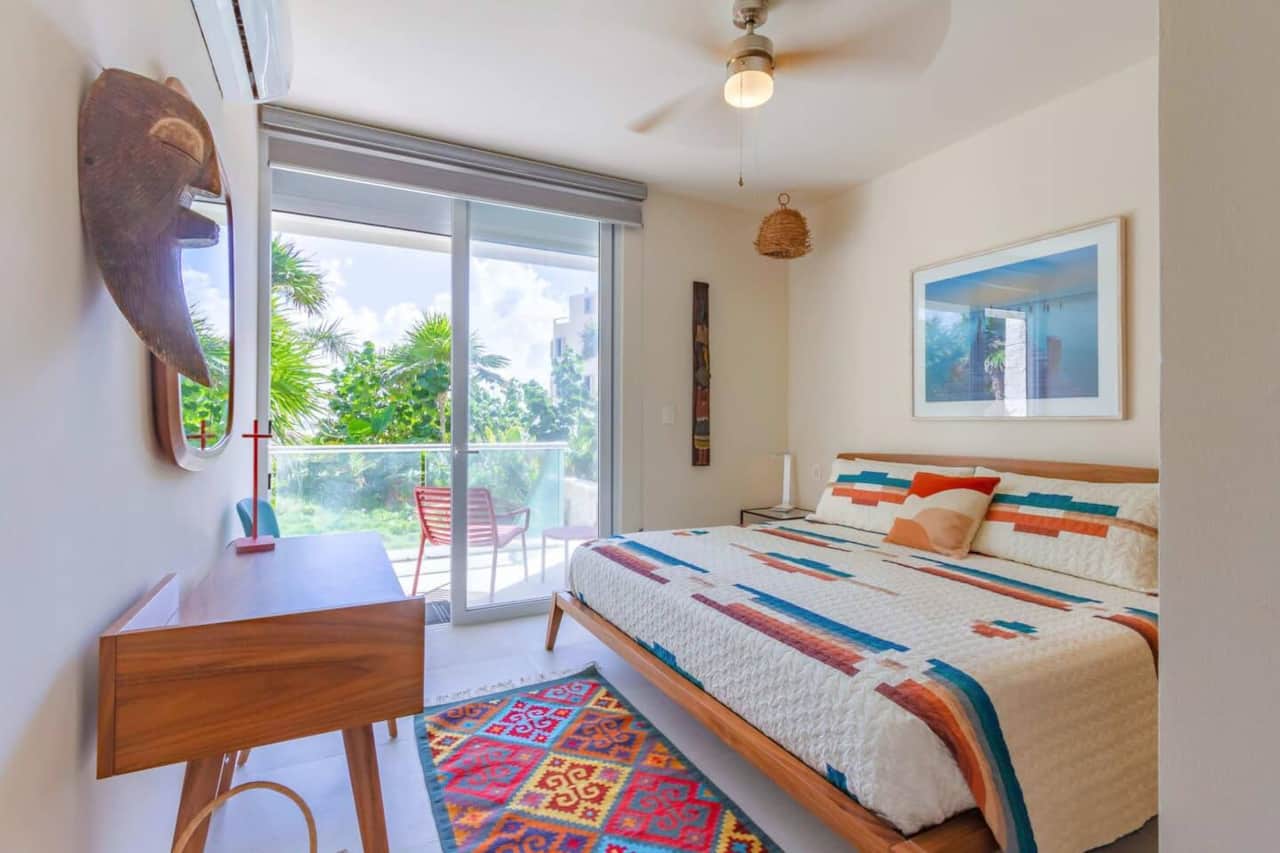 Cozy and colorful bedroom with a king-size bed, air conditioning, ceiling fan, and room-darkening shades. Enjoy lush garden views and direct access to your private terrace with beautiful ocean views—perfect for a peaceful night’s rest.