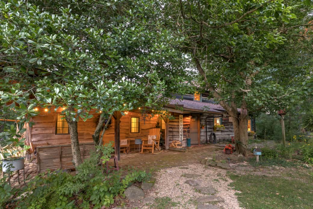 The historic log cabin glows beneath mature trees at dusk