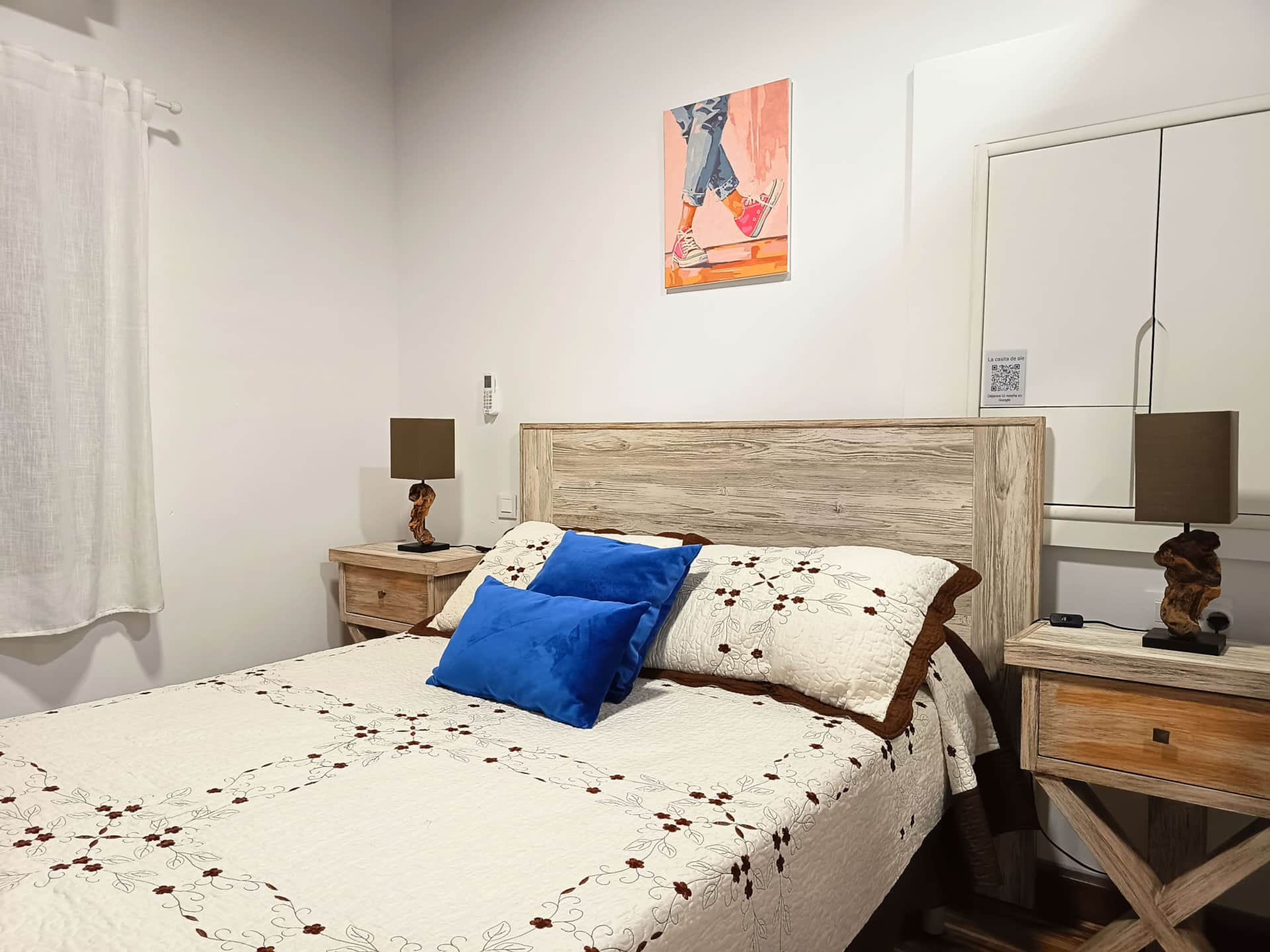 Dormitorio acogedor con cama de cabecero de madera, colcha floral, cojines azules y mesillas con lámparas