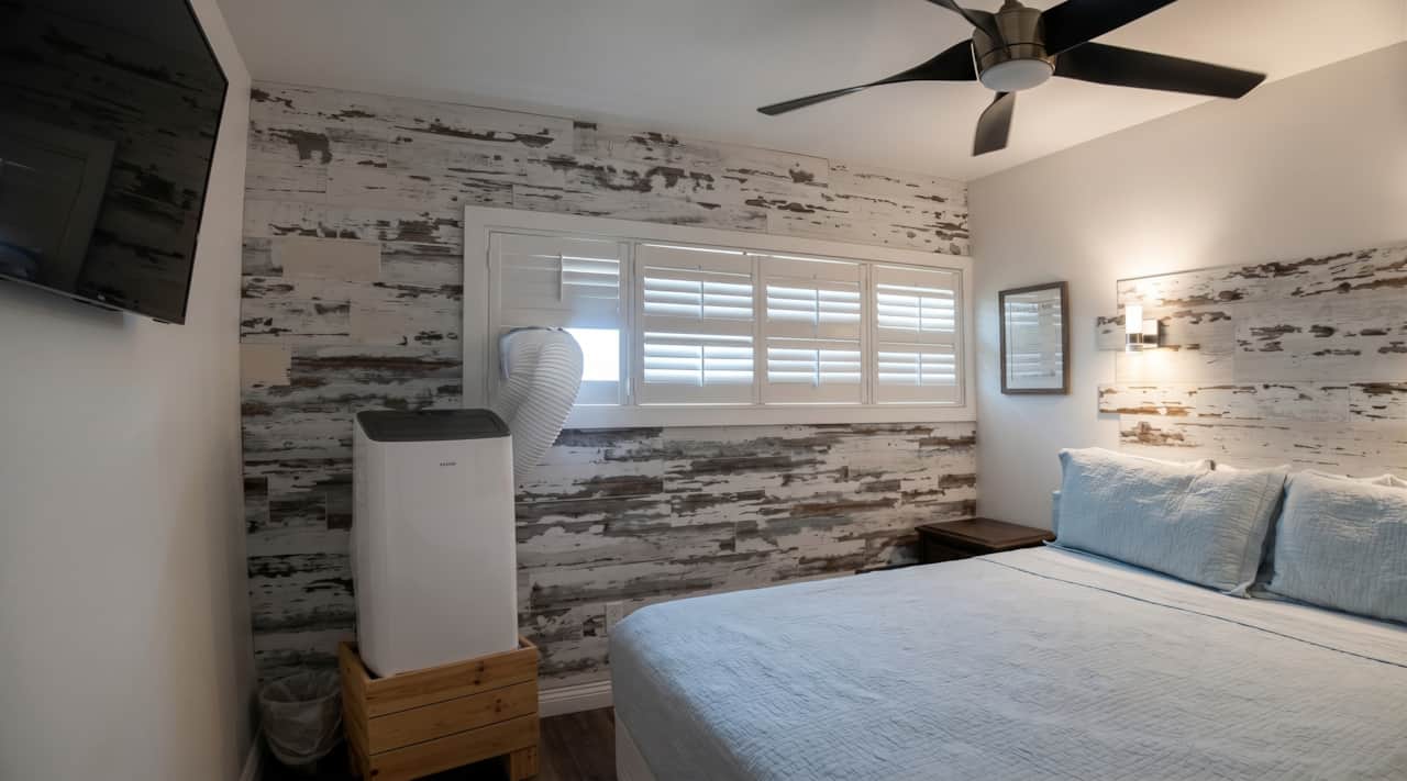 Comfortable bedroom with ceiling fan, TV, plantation shutters, and portable A/C.