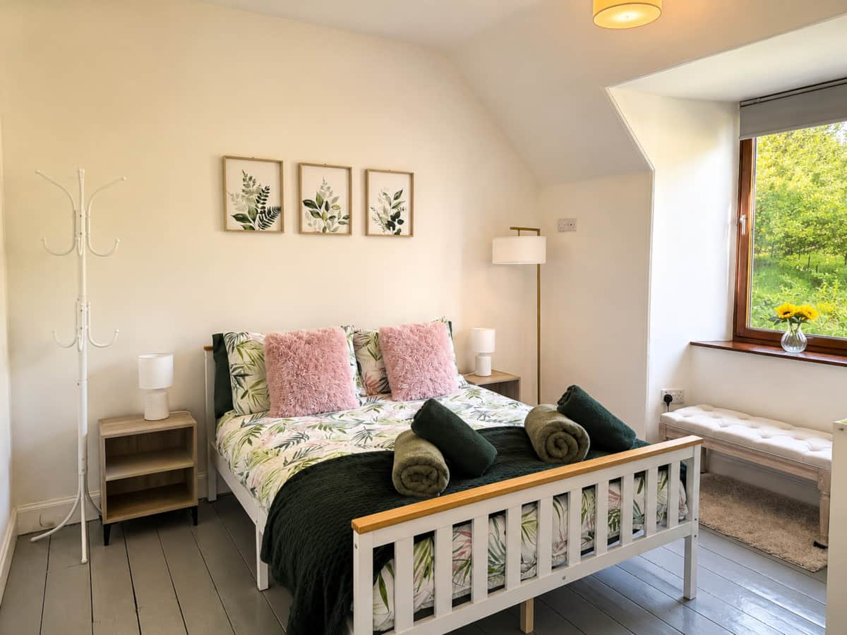 Bedroom 3 with a white wooden bed, botanical linen and a garden view.