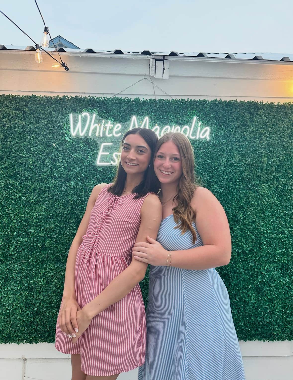 Two teen friends taking photos in front of the White Magnolia Galveston photo wall in the private courtyard