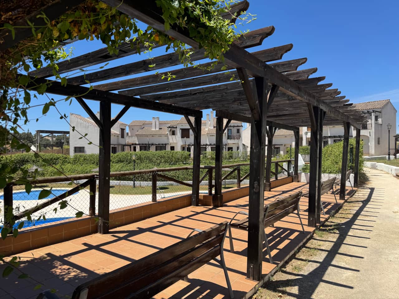 Pérgola con bancos junto a las piscinas de la urbanización