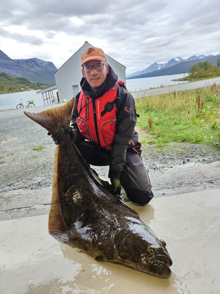Angler kniet mit großem Heilbutt am Fjord