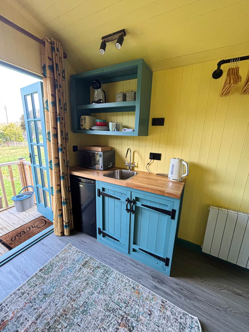 Compact kitchenette with pastel cabinetry and garden views through French doors.