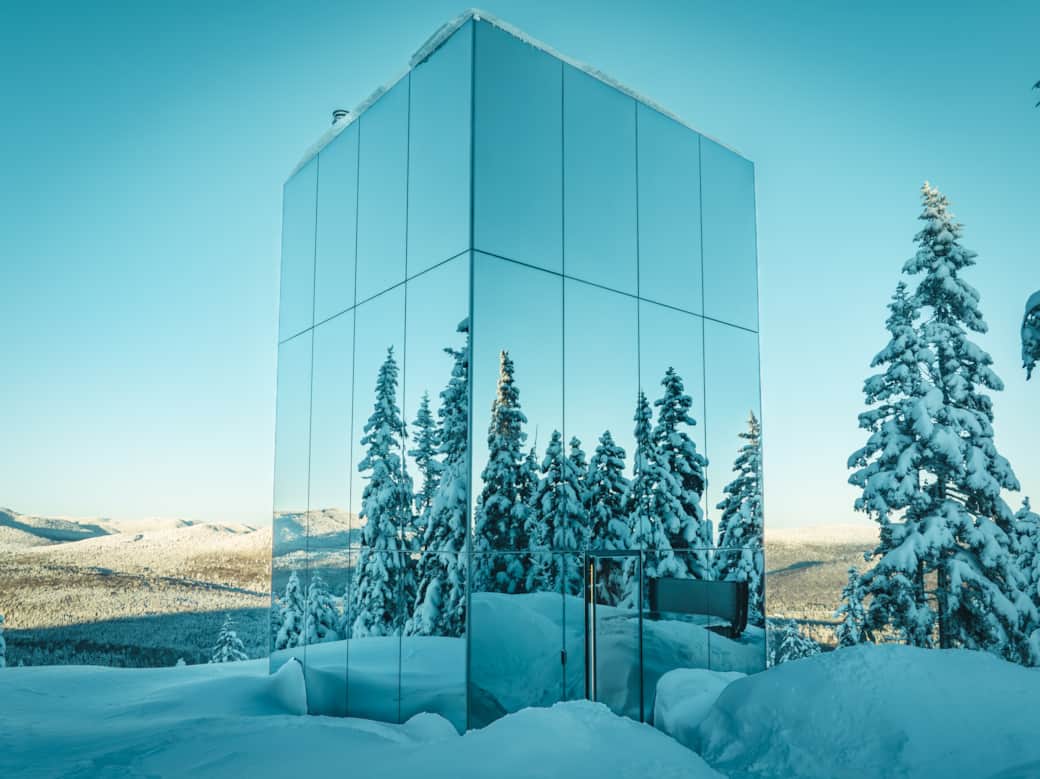 Reflective glass exterior blending into the surrounding forest