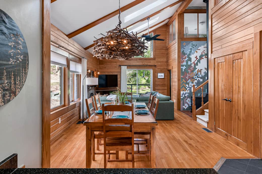 View from kitchen with dining for 6, wood stove on mosaic wall, and light from skylights & doors.
