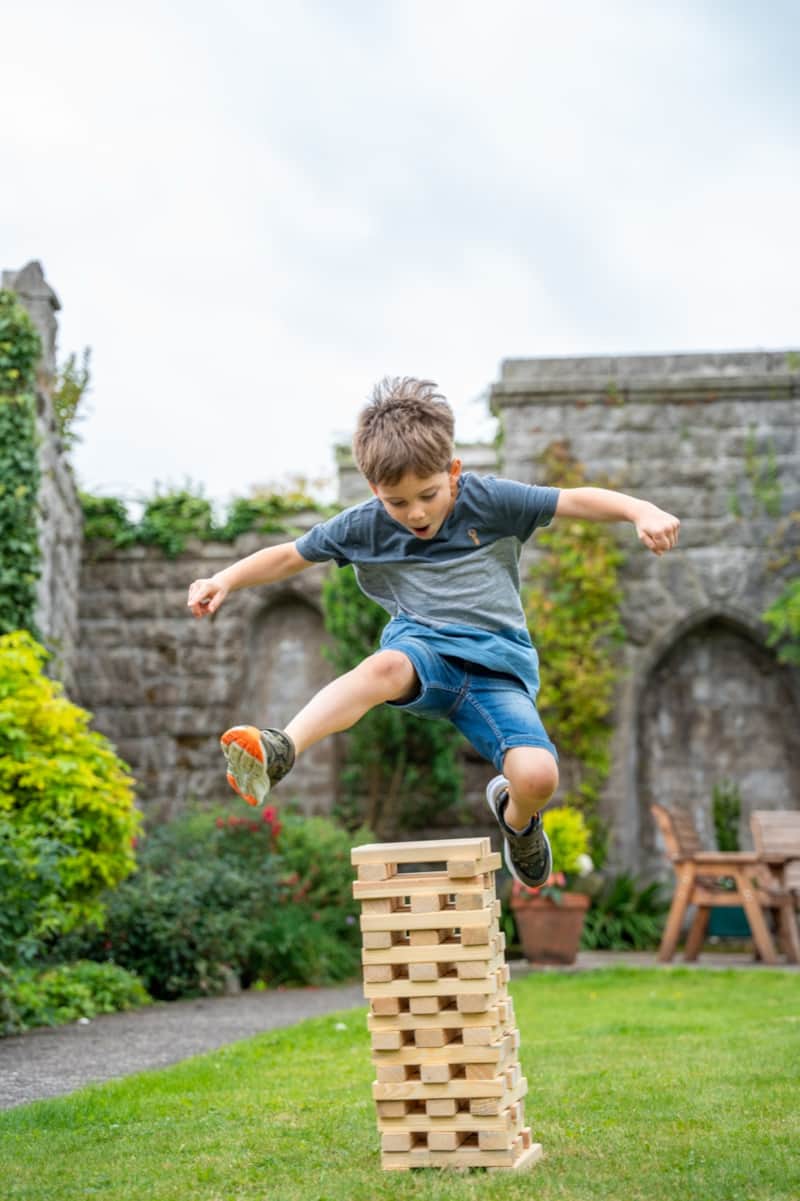 A boy leaping over a tower of wooden blocks in the garden