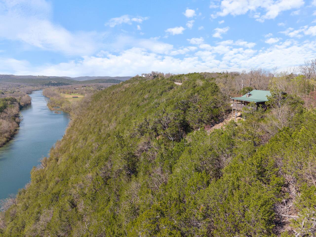 An aerial view of a house with a green roof on a hillside overlooking a river.