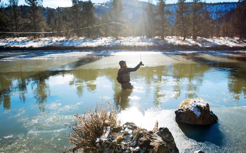 Angler fly fishing in a sunlit mountain river on a winter morning