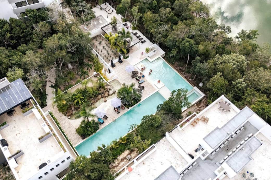 Bird’s-eye view of the complex showcasing resort-style swimming pools, hammocks, outdoor showers, sun umbrellas, and shaded lounge areas, all surrounded by lush jungle greenery, plus a rooftop lounge with elevated views and space to unwind.