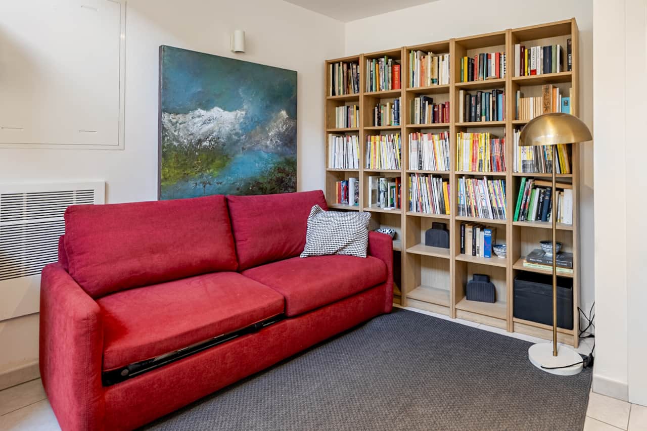 Wohnzimmer mit rotem Sofa, raumhohem Bücherregal und blauem Bild