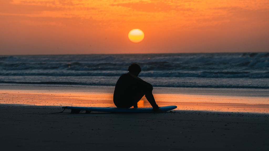 Surfer sitting on the beach at sunset