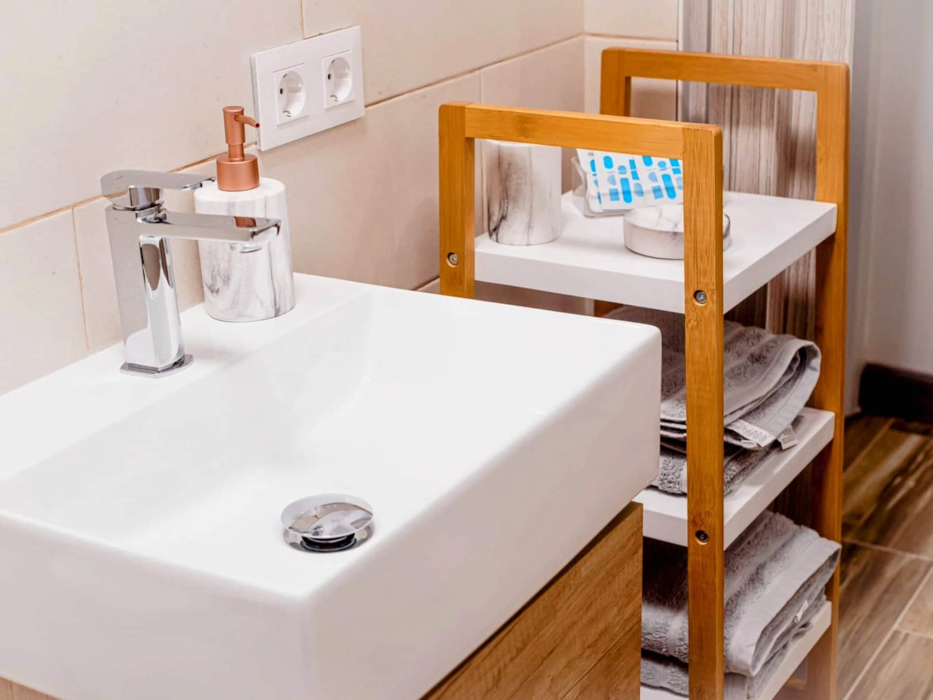 Baño moderno con lavabo rectangular, mueble de madera, estantería con toallas y accesorios de aseo en La Casita de Ale