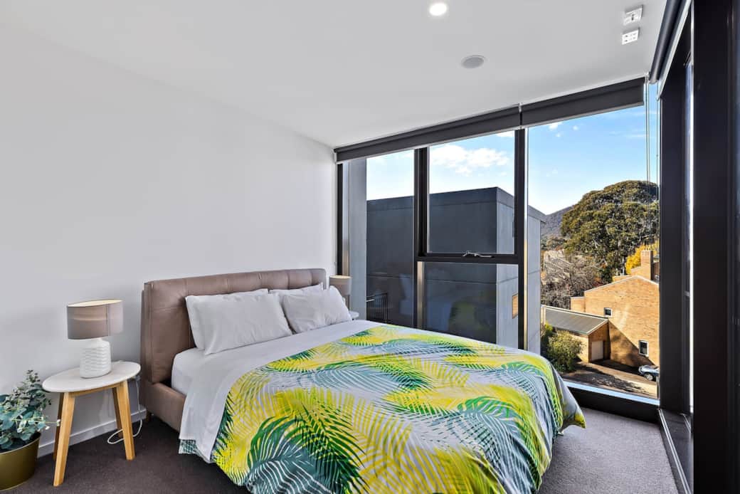 Experience comfort and luxury in this well-appointed bedroom. The bed, dressed in a lively patterned bedspread, is complemented by soft white pillows. The room's large windows offer a stunning view, enhancing the overall elegance of the space.