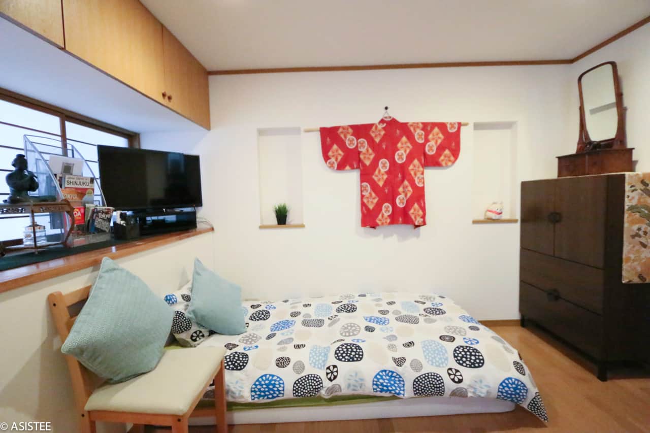 Single futon bed with TV, books and decorative red kimono on wall