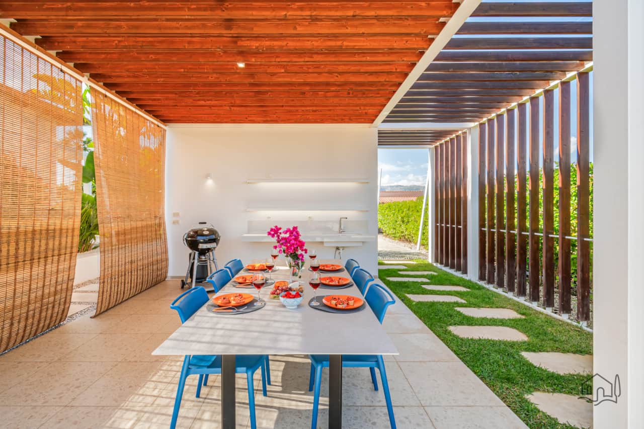 Shaded outdoor dining area with a large table, gas BBQ, and outdoor sink, perfect for relaxed meals.