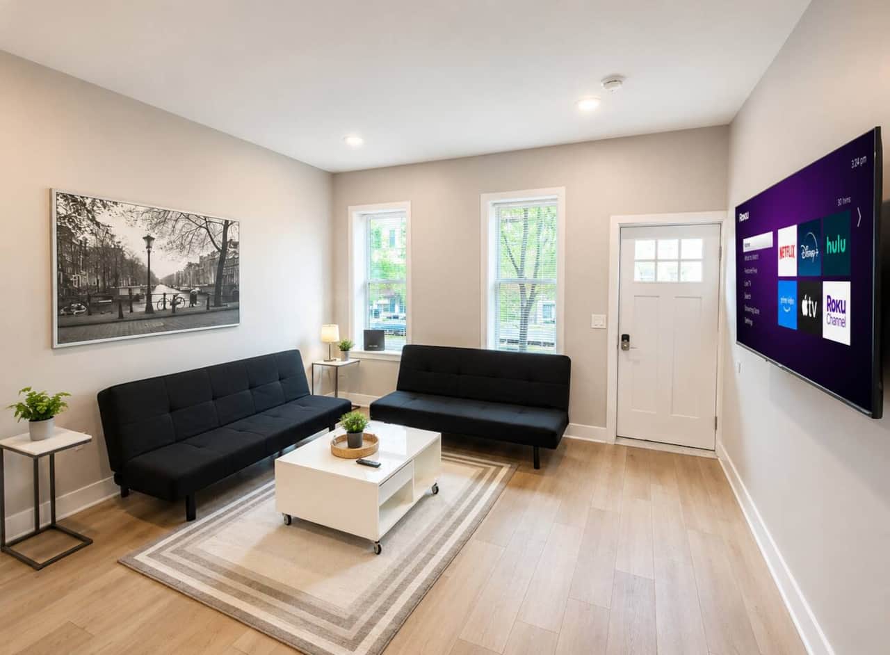 Living room featuring a large flat-screen TV and two comfortable futon sofa beds, providing extra sleeping space for guests. The room flows seamlessly into the fully equipped kitchen with an island and bar seating.