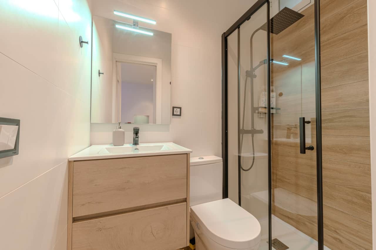 Baño completo con ducha, mampara de cristal y mueble de lavabo