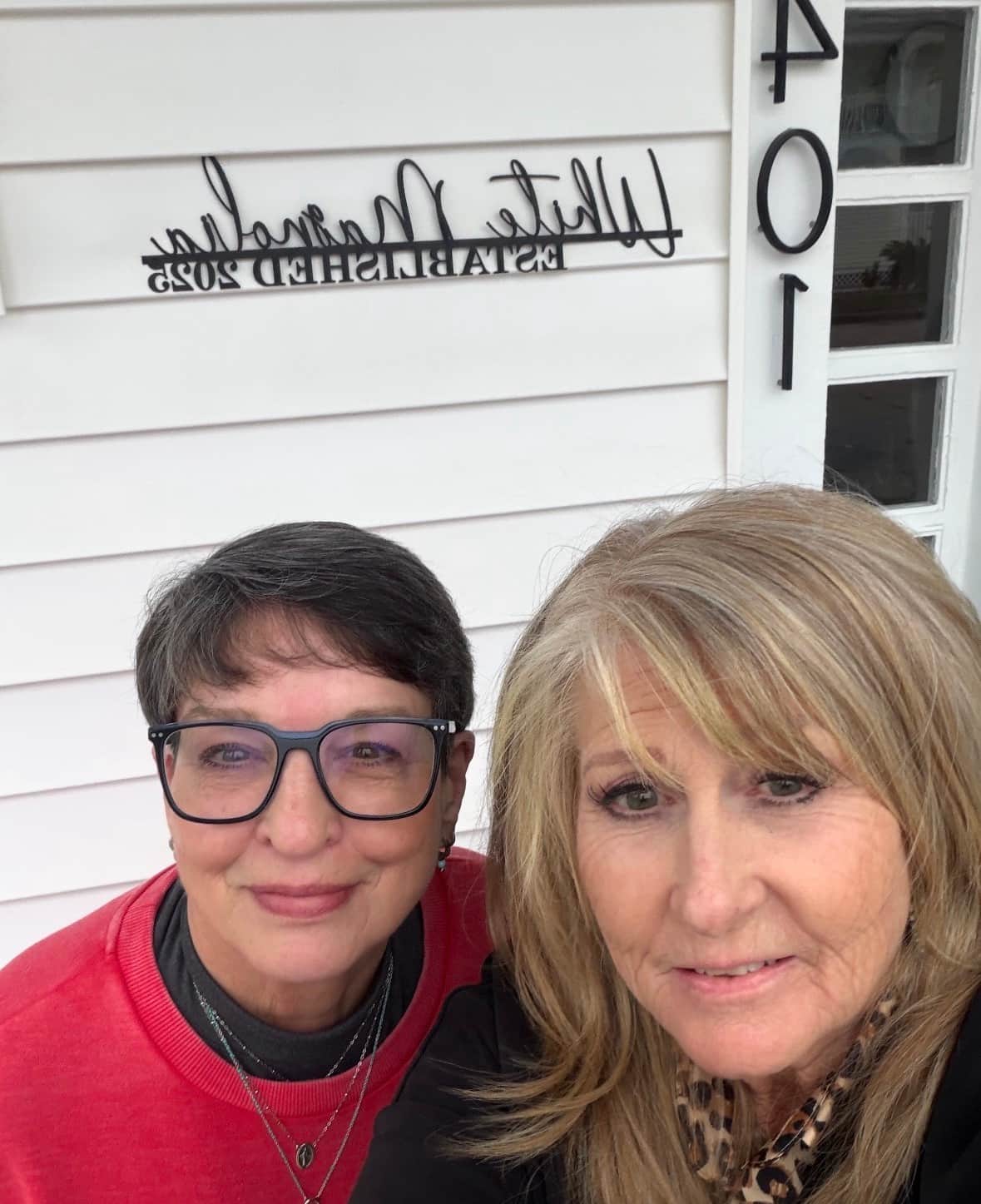 Two friends taking a selfie in front of the White Magnolia Galveston sign by the entry