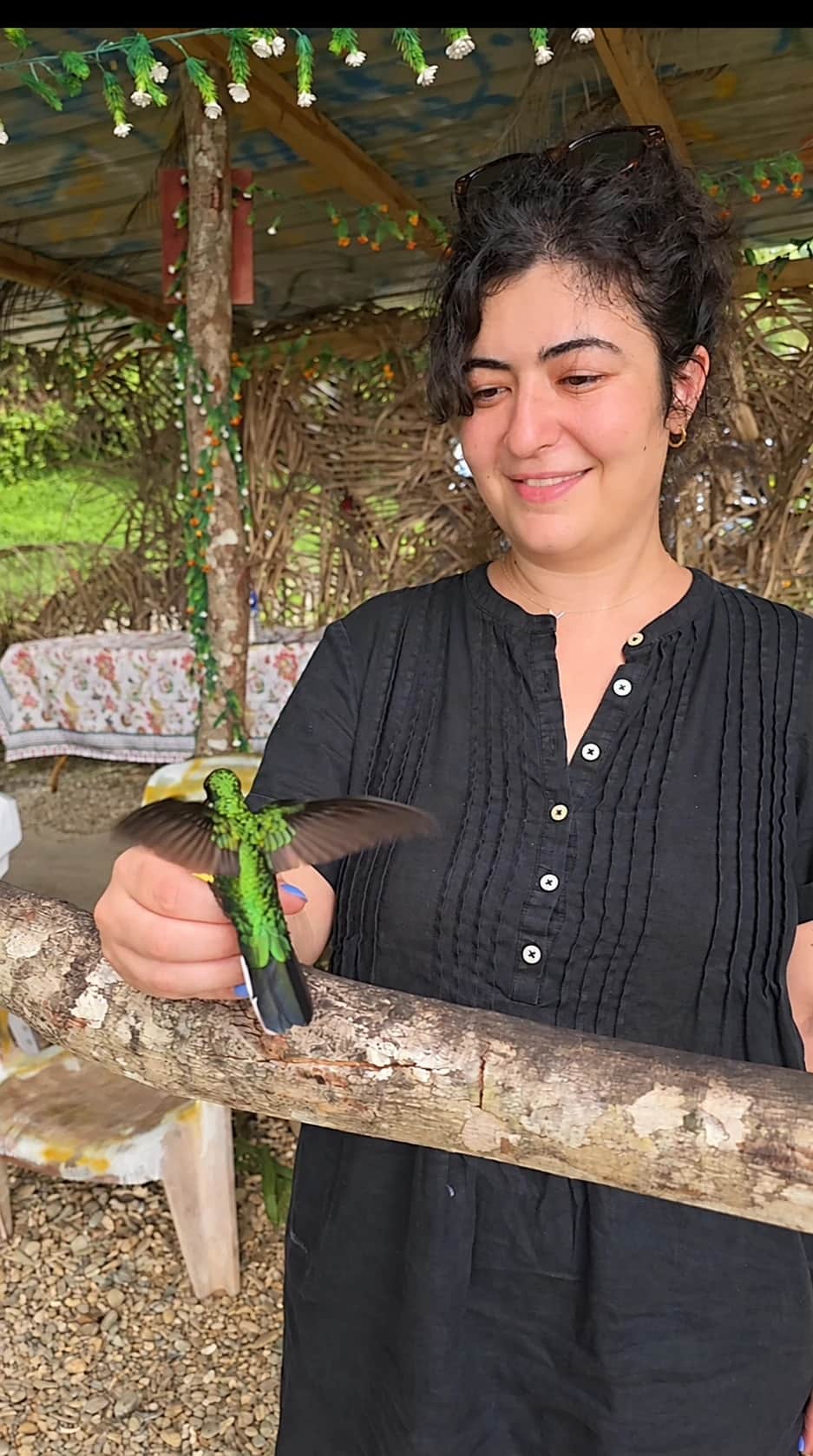 A woman feeding a brilliant green hummingbird by hand in Tobago