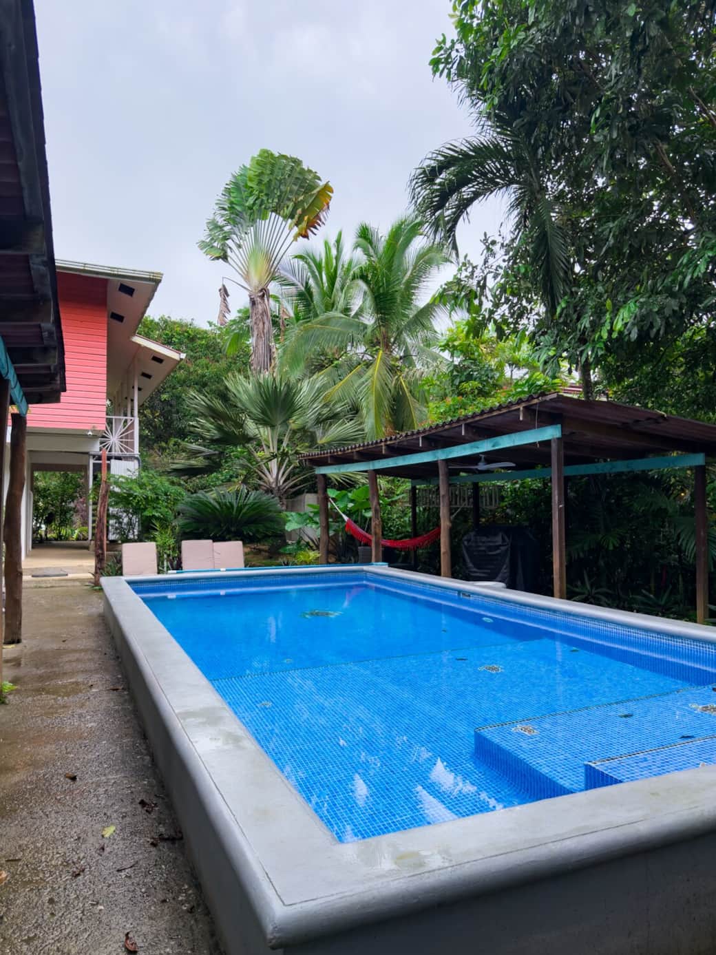 Another angle of the private pool framed by palms and tropical foliage. Covered rancho area includes shaded seating, hammock space, and barbecue for outdoor gatherings.
