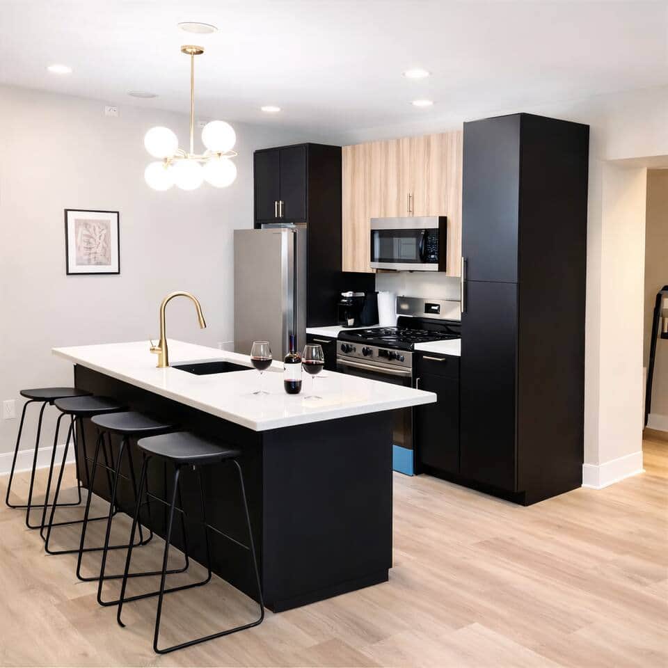 The kitchen counters have been elegantly designed in a sleek black finish. features a large quartz island with barstools. Equipped with appliances, including an oven stove, hood, refrigerator, microwave, dishwasher, and garbage disposal.