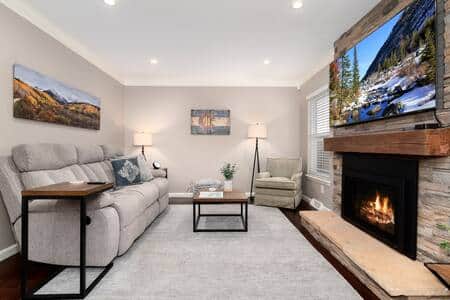 The living room features a comfortable reclining sofa, 65" 4K Television, and gas fireplace. 