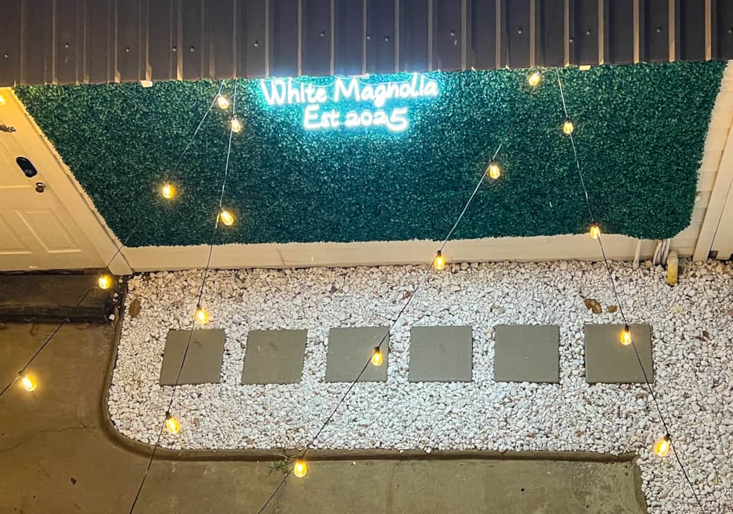 Lighted photo wall in private courtyard with white magnolia neon sign