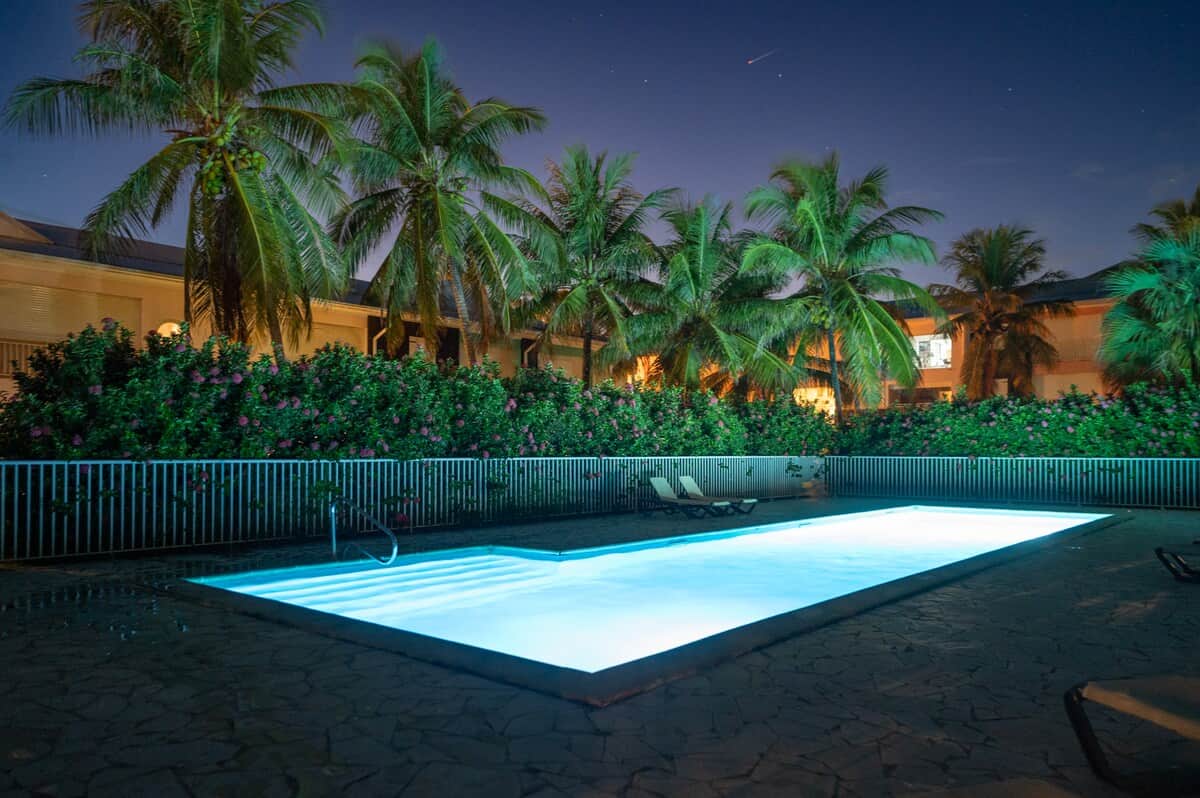Piscine illuminée la nuit, palmiers et résidence