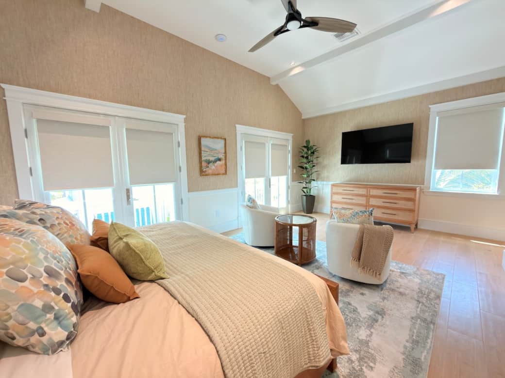 A spacious upstairs primary suite with a king bed, vaulted ceiling, smart TV, ceiling fan, and a private sitting area. Finished in a refined coastal-modern style, it also features a private balcony overlooking the pool and a luxurious en-suite bath.