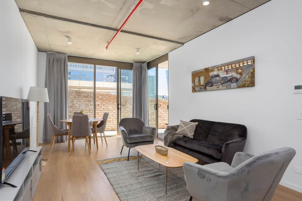 Welcome to your urban retreat, where contemporary design meets comfort. Our living room, bathed in natural light from expansive windows, offers a serene space to unwind after a day of exploration