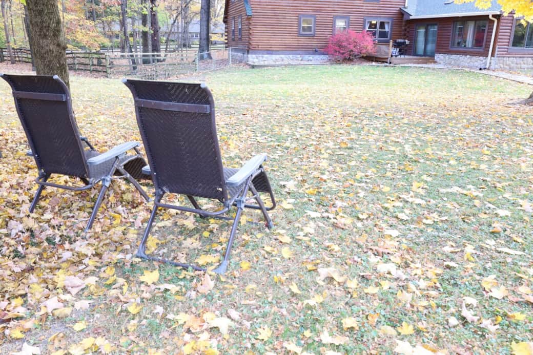 Relax outdoors with lounge chairs overlooking the spacious yard, surrounded by mature trees and peaceful cabin vibes.