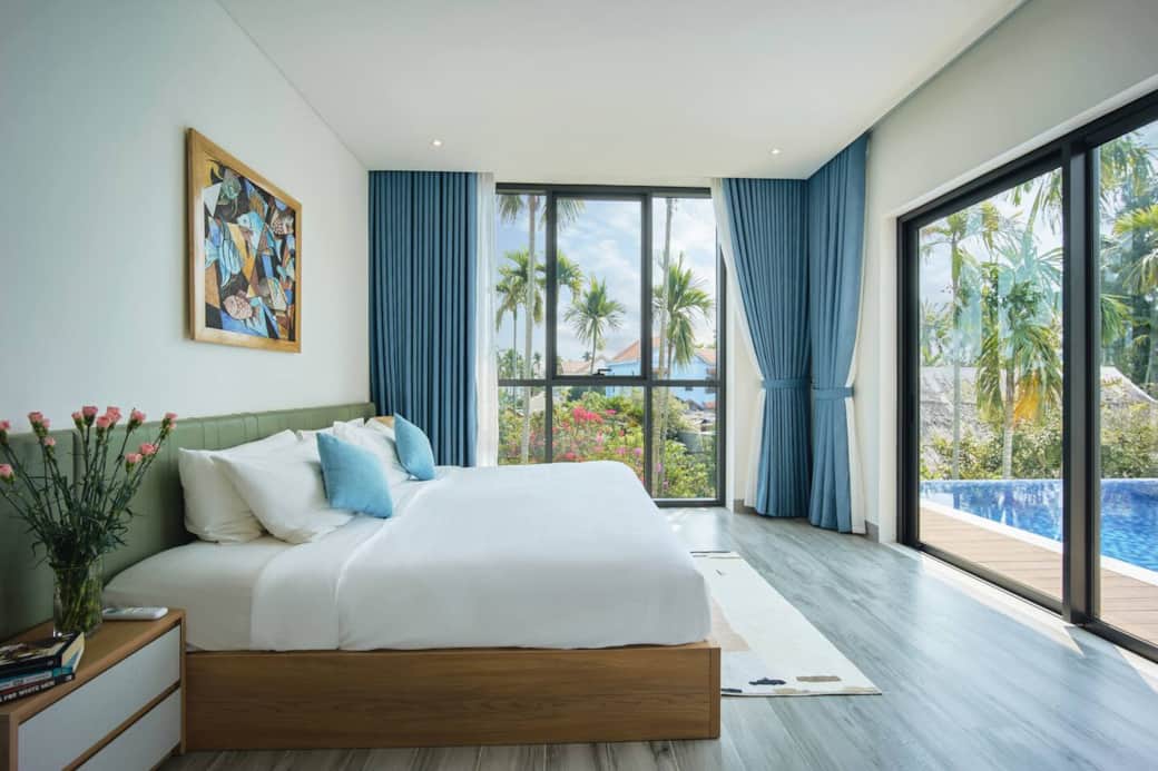 The master bedroom features a king-size bed and spacious layout, complemented by two large windows that offer stunning views of the pool and river, creating a serene water-on-water visual experience.