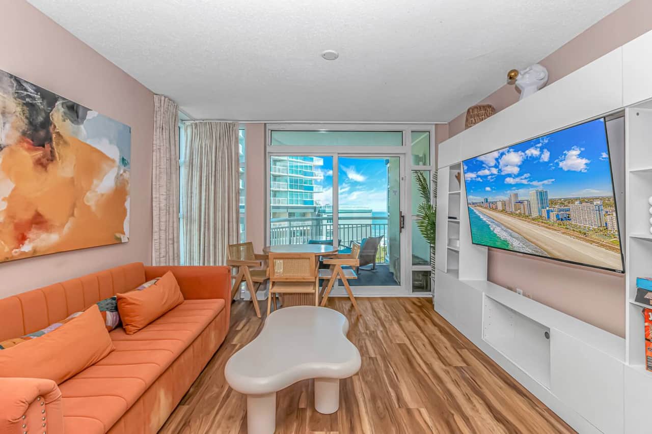 Modern beach vibes — stylish living room with smart TV, dining space, and balcony access for the perfect coastal retreat 