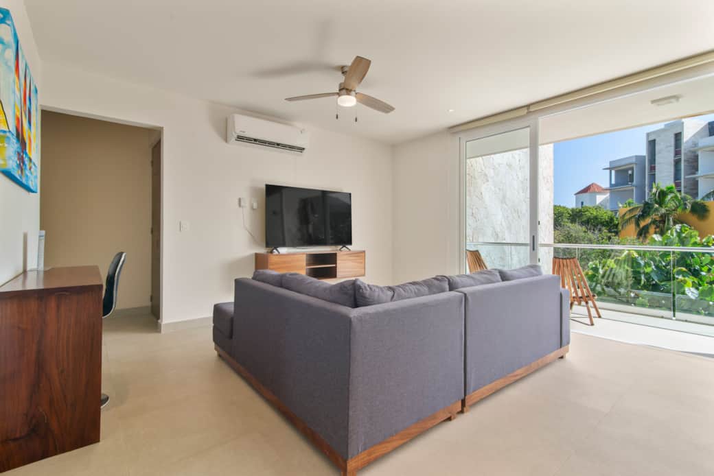 Cozy living room with plush couch, smart TV, AC, fan & balcony access.